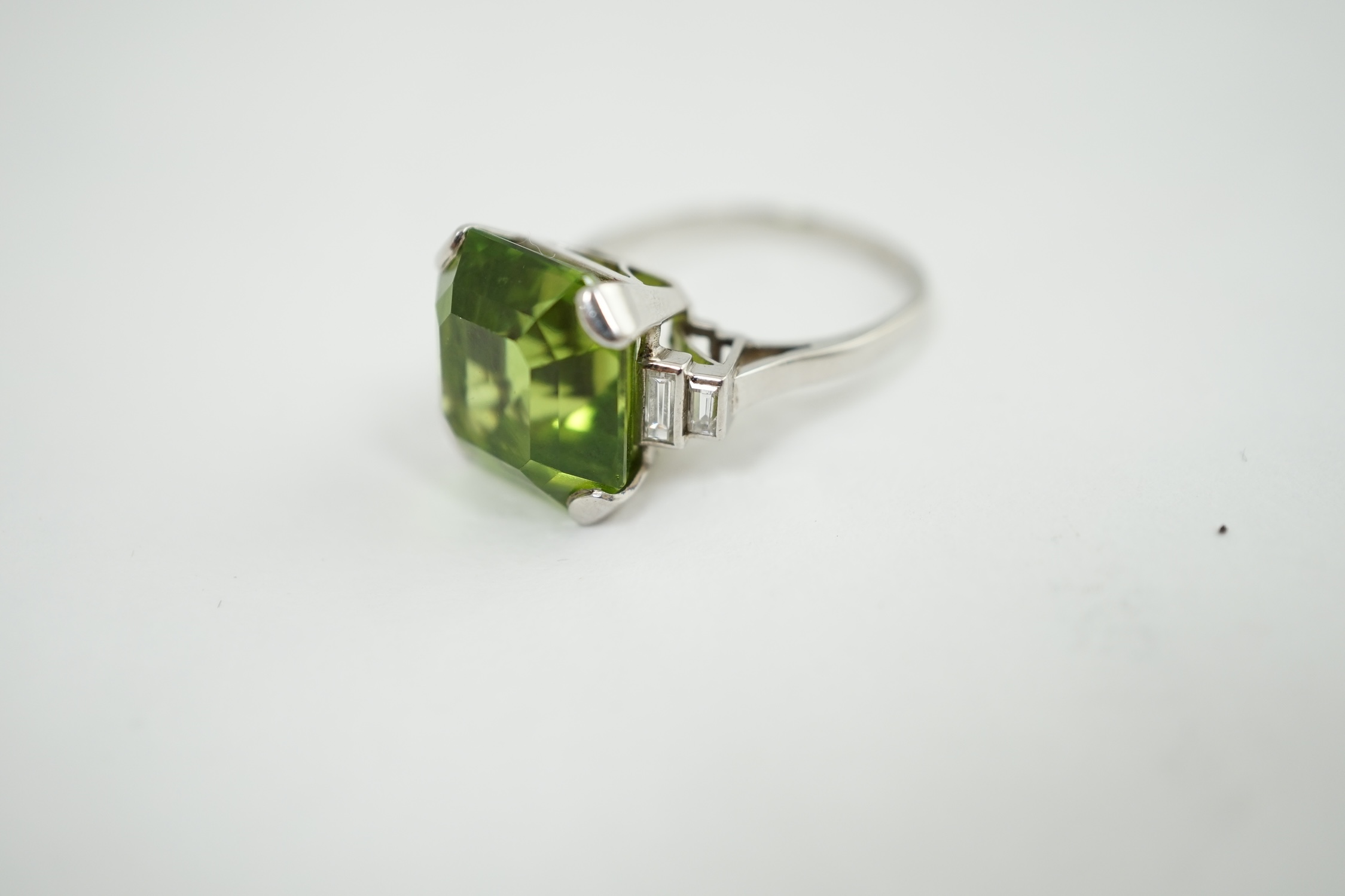 A 1920's platinum and single stone asscher cut peridot set dress ring, with four stone graduated baguette cut diamond set shoulders